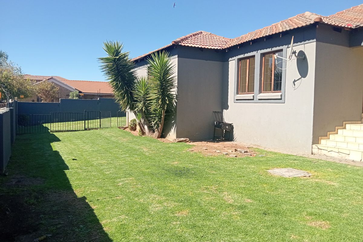 A rear view of the property featuring a private garden, lawn area, perimeter walling, and external concrete stairs leading to the house.
