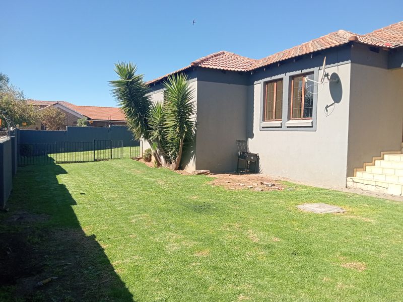 A rear view of the property featuring a private garden, lawn area, perimeter walling, and external concrete stairs leading to the house.