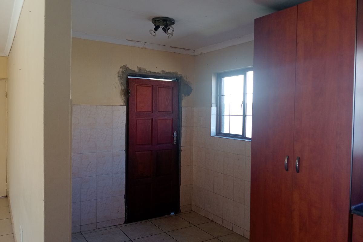 A kitchen area featuring tiled walls and flooring, built-in cabinetry, and a wooden door, currently requiring cosmetic repairs to the plasterwork and ceiling.
