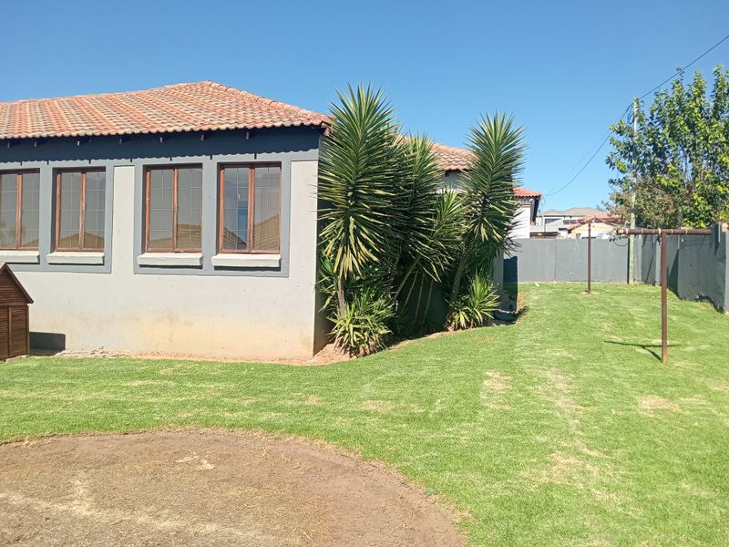 Rear view of the property featuring a plastered exterior, tiled roof, timber-framed windows, and a private garden area with a boundary wall.