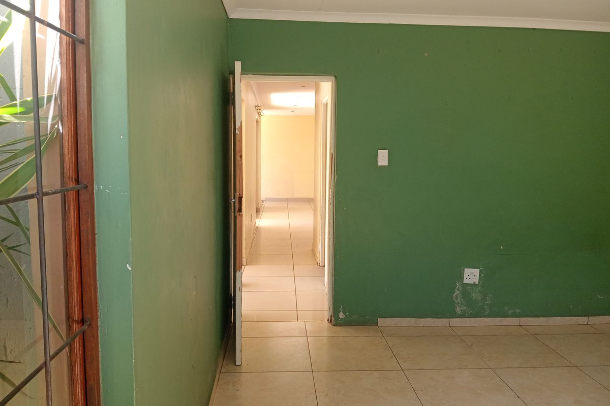An empty living room featuring tiled flooring, green painted walls, and a doorway leading to a hallway.
