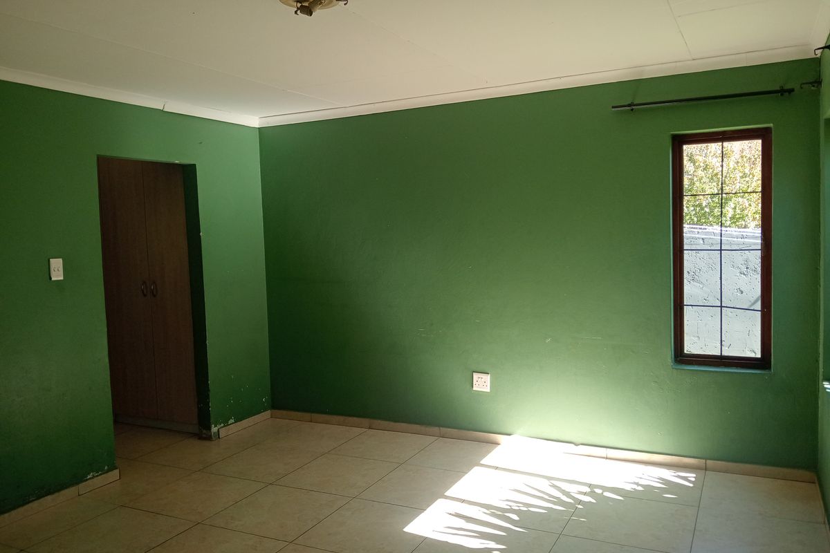 An empty bedroom featuring tiled flooring, a built-in cupboard, and a window with burglar bars, finished with green painted walls.