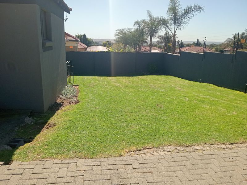 A private rear garden featuring a well-maintained lawn, enclosed by high perimeter walls with integrated electric fencing and a paved area.