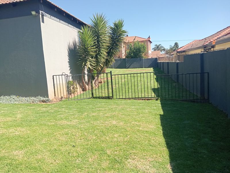 A well-maintained rear garden featuring a manicured lawn, enclosed by perimeter walls and metal fencing.