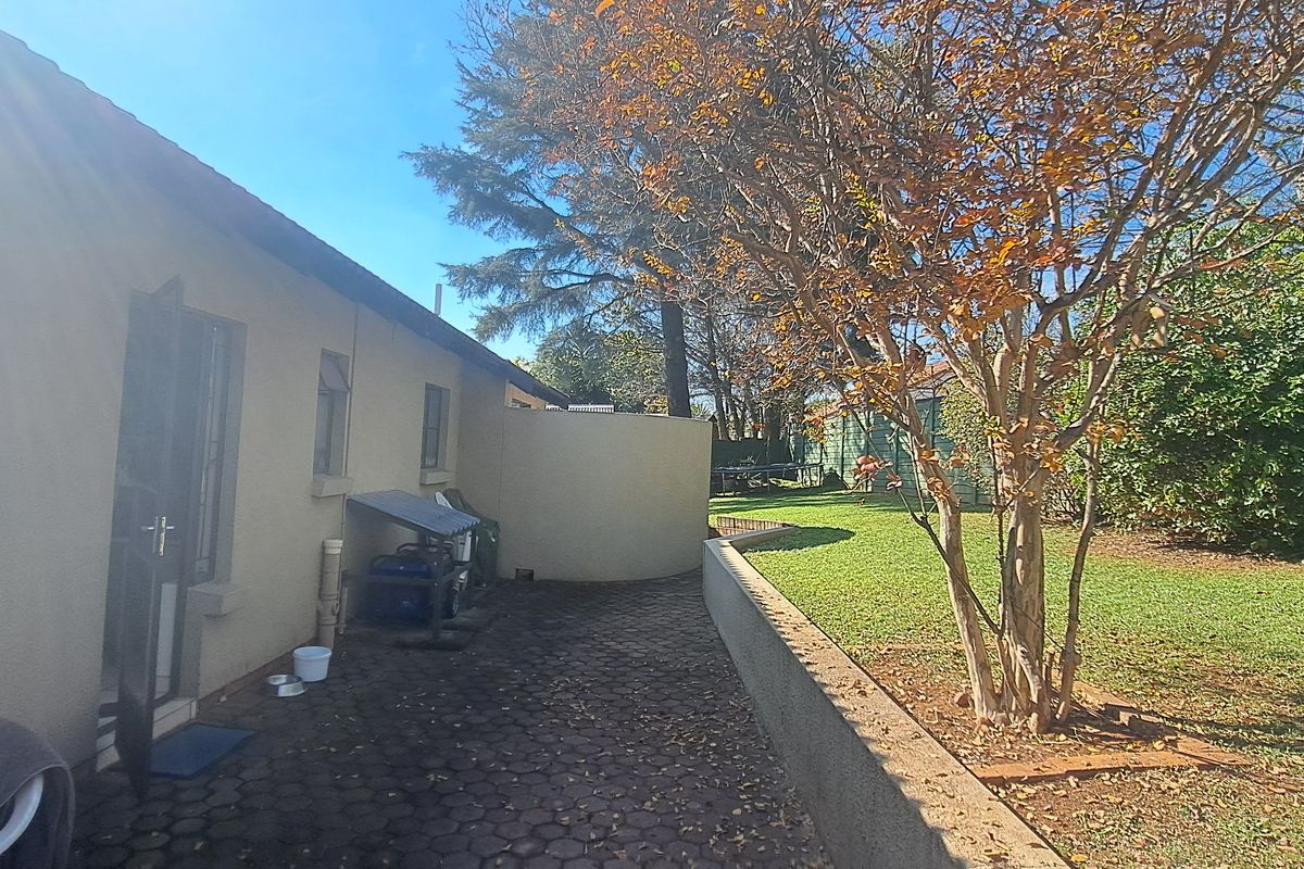 A view of the rear exterior featuring a paved patio area, a low retaining wall, and a landscaped garden with mature trees.