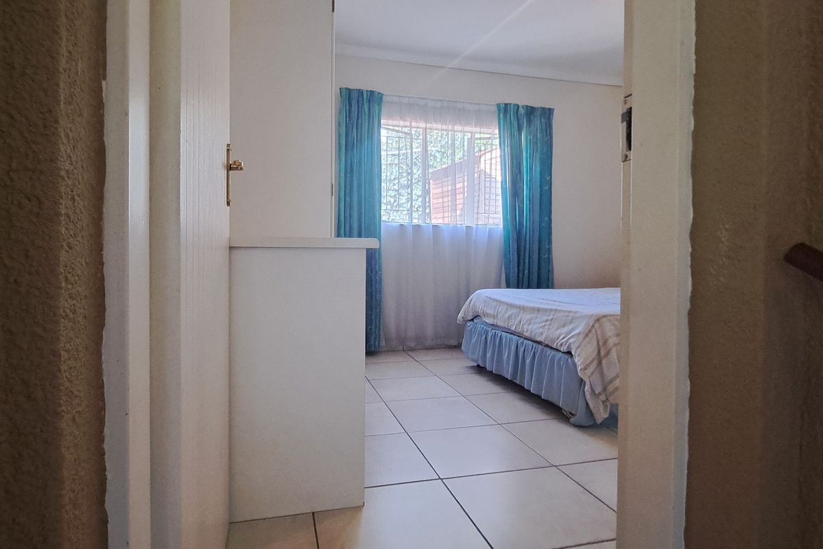A view into a bedroom featuring tiled flooring and a window with security bars, accessed through a doorway from a hallway.