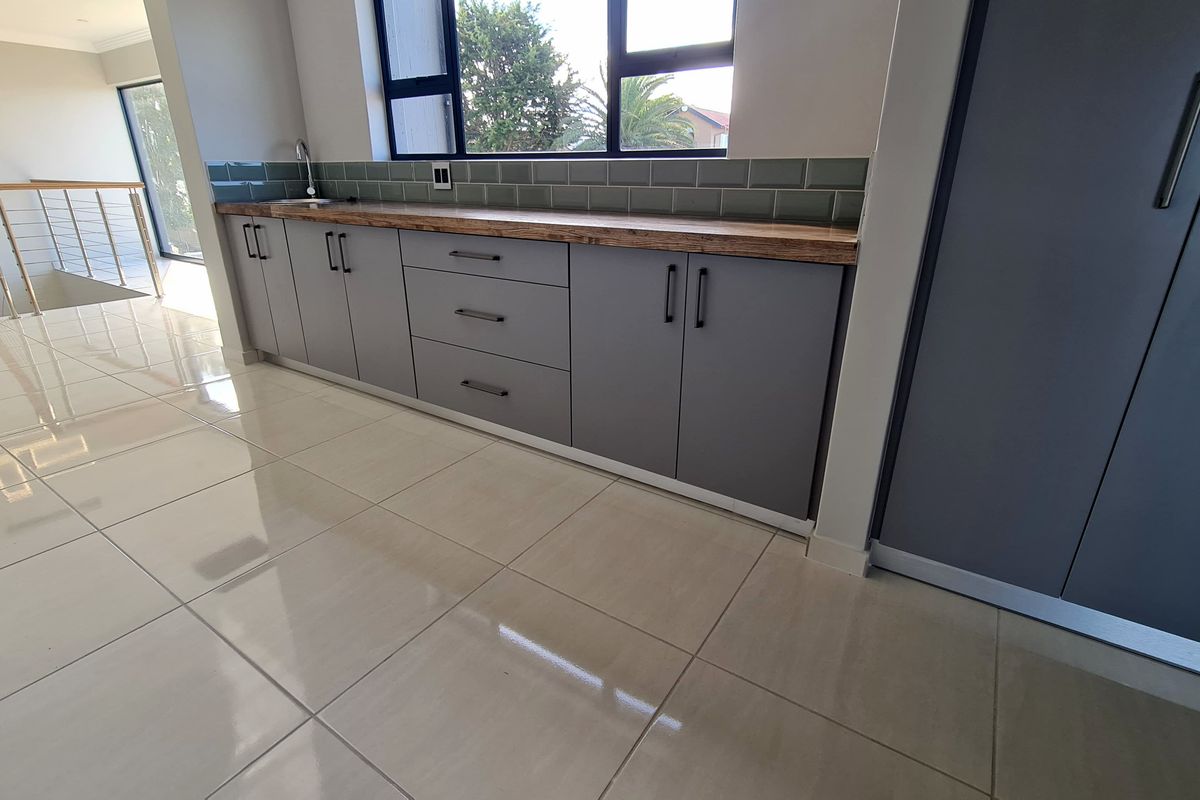 Modern kitchen area featuring sleek grey cabinetry, a natural wood countertop, subway tile backsplash, and polished porcelain floor tiles.