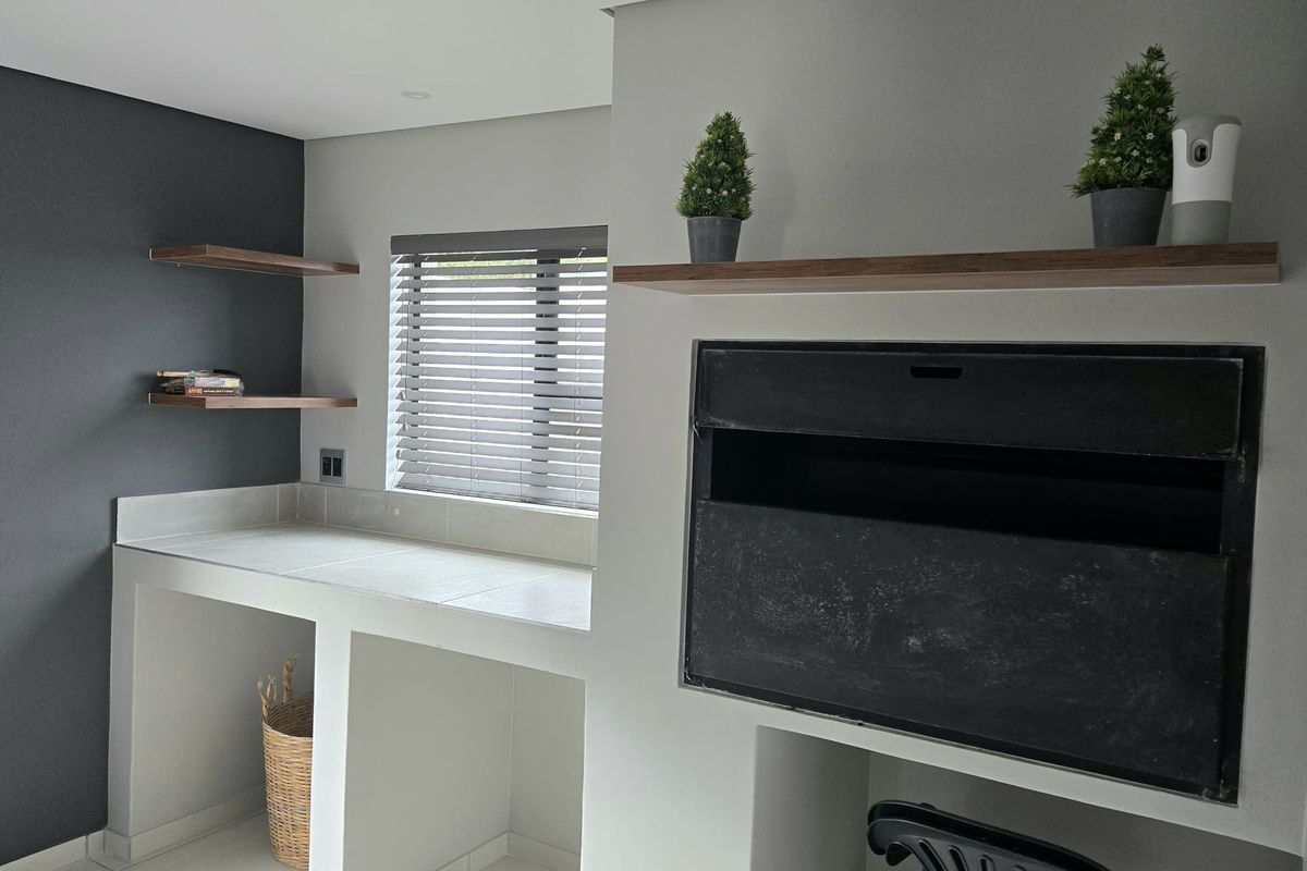 A modern living area featuring a built-in fireplace, floating wooden shelves, and a tiled workspace with neutral grey and white finishes.