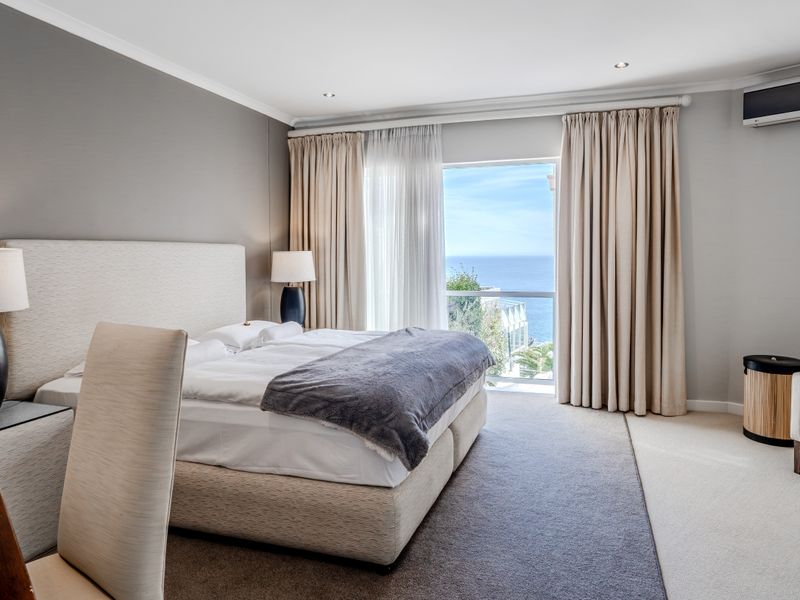 A well-appointed bedroom featuring neutral tones, carpeted flooring, recessed lighting, and a wall-mounted air conditioning unit with a view of the ocean.