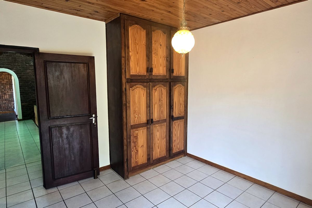 A bedroom featuring a built-in wooden wardrobe, tiled flooring, and a wooden ceiling, with an arched doorway leading to an adjacent space.