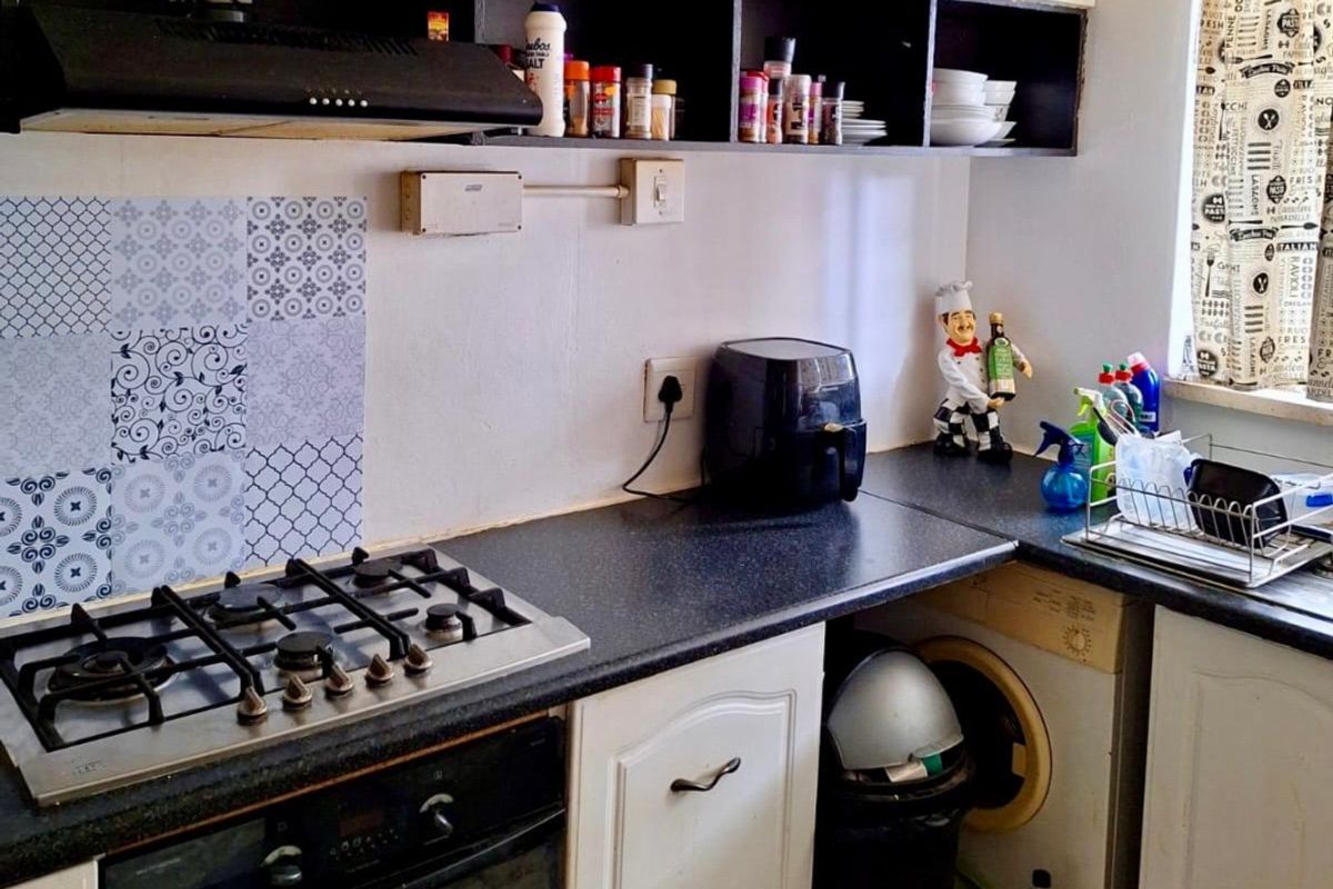 A functional kitchen featuring a gas hob, built-in oven, extractor fan, and under-counter space for a washing machine with tiled splashback detailing.