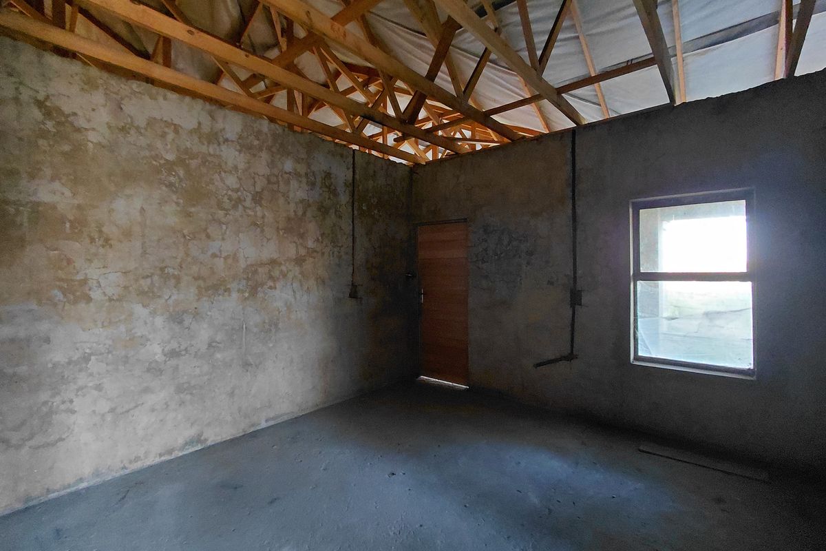 An unfinished room in shell condition featuring exposed timber roof trusses, concrete flooring, and unplastered masonry walls, awaiting completion and interior finishes.