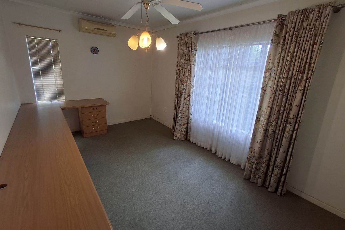 A functional bedroom featuring a built-in desk, ceiling fan, and split-system air conditioning unit, offering a versatile space for a home office or bedroom.