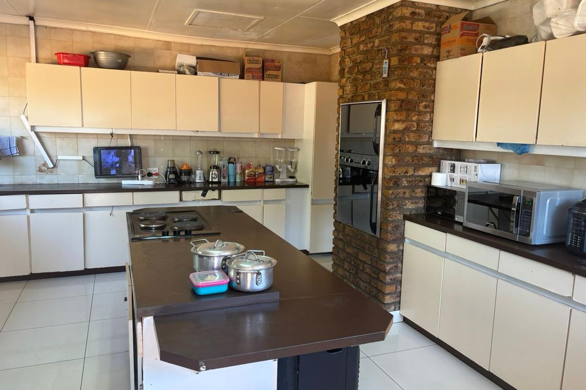 Spacious kitchen featuring an island, built-in oven, gas hob, and a distinctive exposed brick feature wall with ample storage cabinetry.