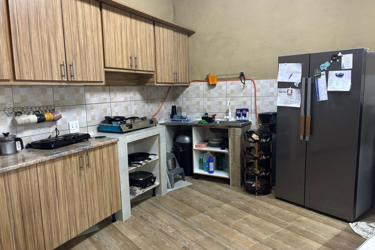 A functional kitchen featuring wood-look laminate cabinetry, tiled backsplash, and tiled flooring, requiring some cosmetic updates to the cabinetry and wall finishes.