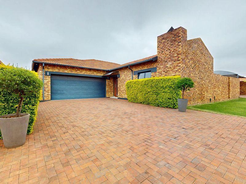 Front elevation of a facebrick cluster home featuring a paved driveway, double garage, and a prominent chimney stack.