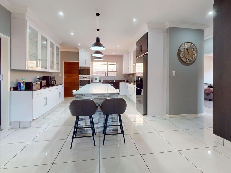 Modern kitchen featuring a central island with stone cladding, sleek white cabinetry, built-in appliances, and polished tiled flooring.