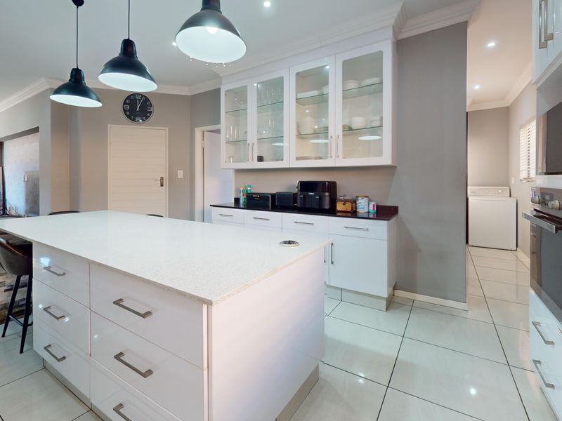 Modern kitchen featuring a large central island with quartz countertops, sleek white cabinetry, built-in appliances, and elegant pendant lighting.