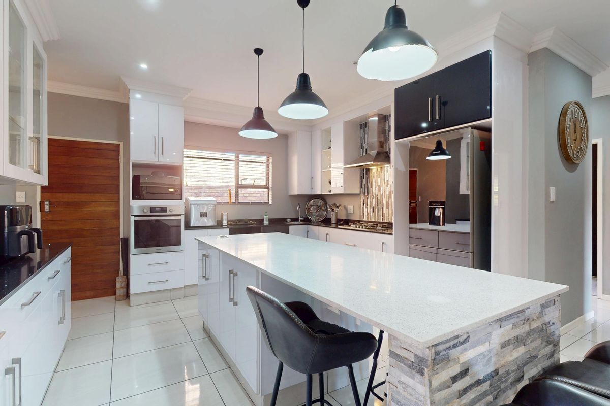 Modern kitchen featuring a large central island with quartz countertops, built-in oven, gas hob, extractor fan, and stylish stone cladding detail.