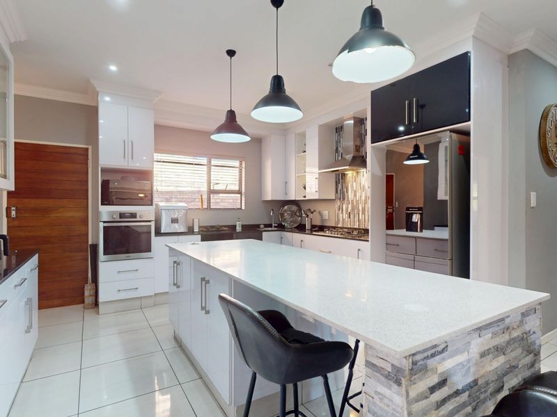 Modern kitchen featuring a large central island with quartz countertops, built-in oven, gas hob, extractor fan, and stylish stone cladding detail.