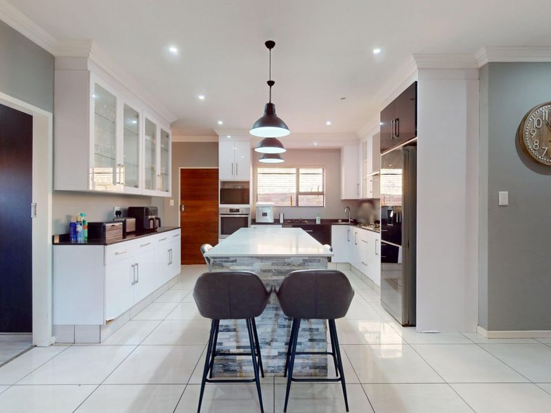 Modern kitchen featuring a central island with stone countertop, glass-front cabinetry, built-in appliances, and sleek tiled flooring with recessed and pendant lighting.