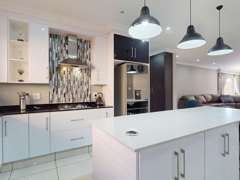 Modern open-plan kitchen featuring a central island, sleek white cabinetry, quartz countertops, and a stylish mosaic backsplash, seamlessly flowing into the living area.