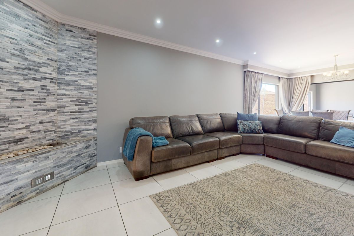 Spacious living room featuring a modern stacked stone feature wall, neutral tiled flooring, and recessed downlighting, creating a comfortable and contemporary atmosphere.