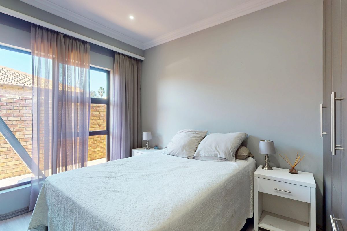 A well-maintained bedroom featuring neutral wall tones, built-in cupboards, elegant cornicing, and a large window allowing for ample natural light.