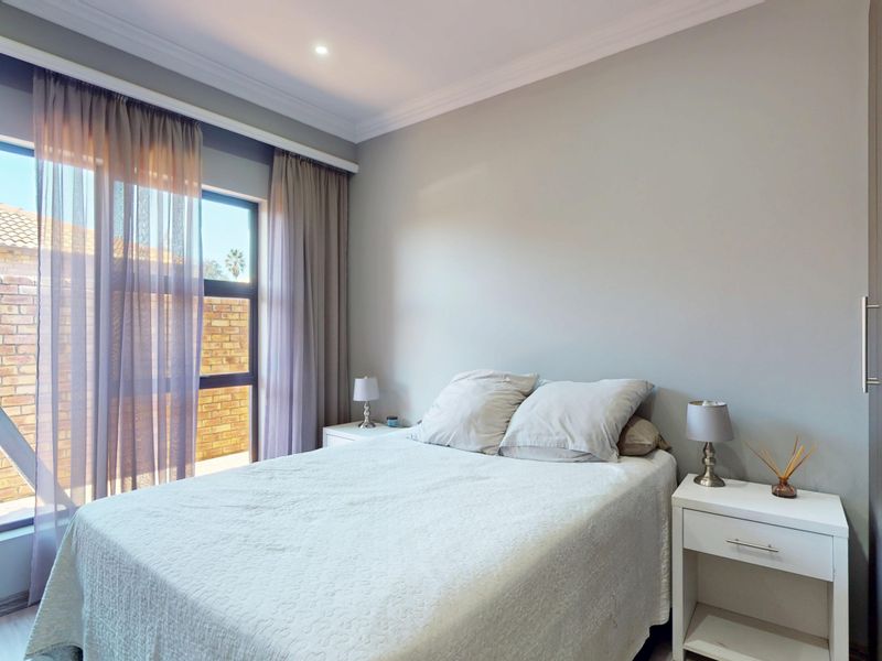 A well-maintained bedroom featuring neutral wall tones, built-in cupboards, elegant cornicing, and a large window allowing for ample natural light.