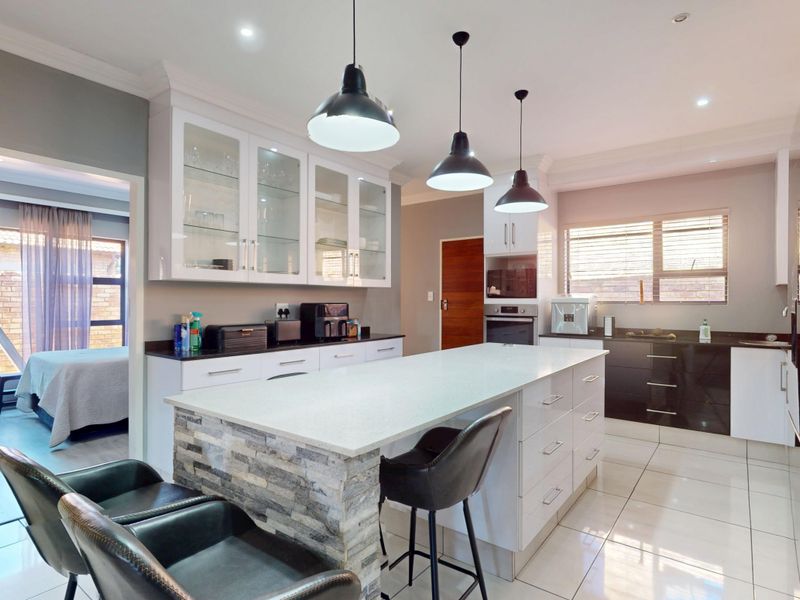 Modern kitchen featuring a central island with stone cladding, quartz countertops, glass-front cabinetry, and high-quality built-in appliances with sleek tiled flooring.