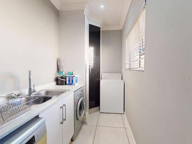 A clean and functional laundry room featuring built-in cabinetry, a stainless steel sink, tiled flooring, and space for laundry appliances.