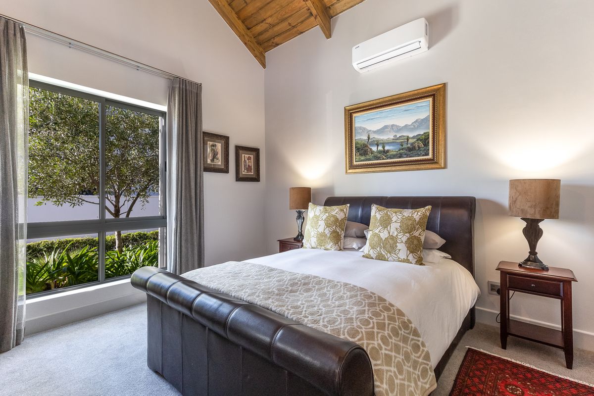 A well-maintained bedroom featuring a vaulted timber ceiling, split-system air conditioning, and a large window providing natural light and garden views.
