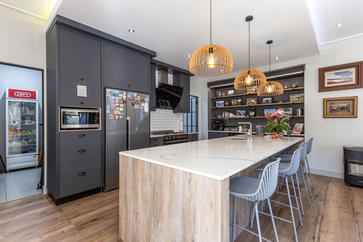 Modern kitchen featuring a large central island with quartz countertops, dark cabinetry, subway tile backsplash, and high-quality built-in appliances.