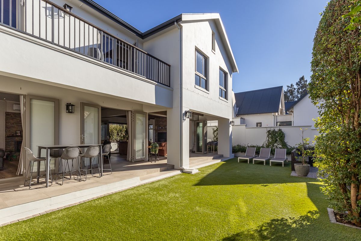 A well-maintained rear exterior featuring a covered patio with bi-fold doors, a balcony with metal railings, and a neat artificial lawn garden.