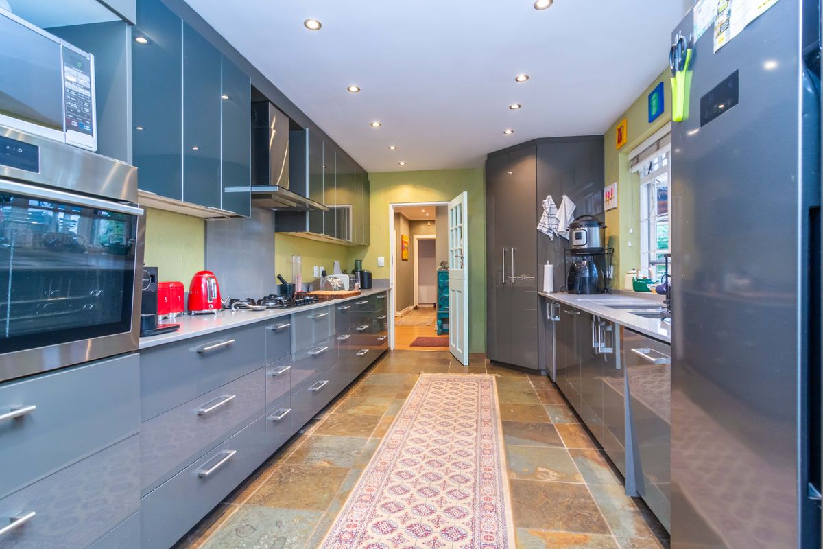 Modern galley-style kitchen featuring high-gloss cabinetry, built-in appliances, stone tile flooring, and recessed lighting.