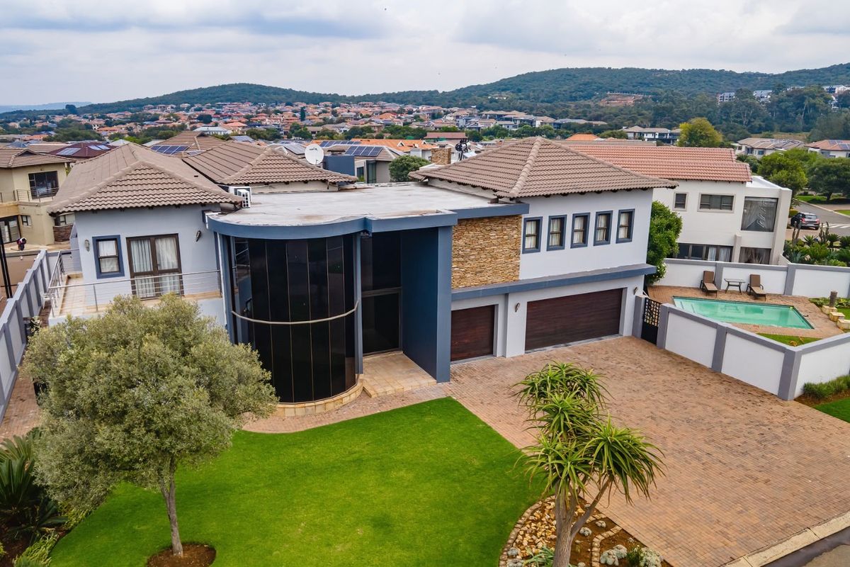 Aerial view of a modern double-story residence featuring a paved driveway, double garage, swimming pool, and contemporary architectural stone and glass detailing.
