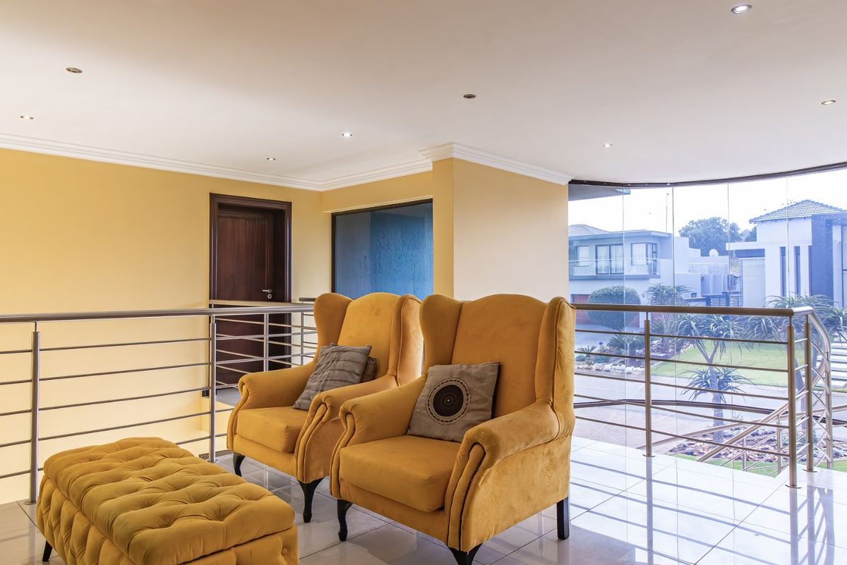 A bright landing or living area featuring a curved glass wall, stainless steel balustrade, and modern recessed lighting with views over the estate.