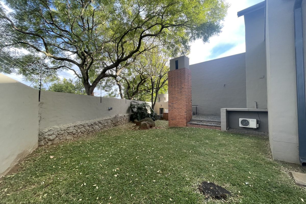 A private rear garden featuring a brick outdoor fireplace, stone retaining wall, paved patio section, and established trees within a secure walled perimeter.