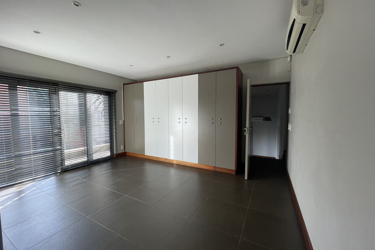 Spacious bedroom featuring large built-in cupboards, tiled flooring, split-system air conditioning, and sliding glass doors with venetian blinds.