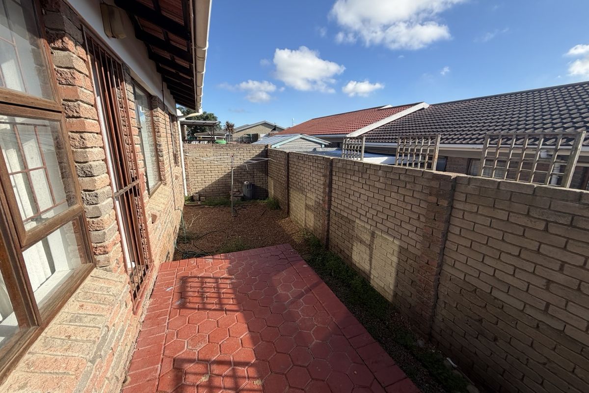 A rear exterior view of the townhouse featuring a paved patio area, brick boundary walls, and a small gravel garden section.