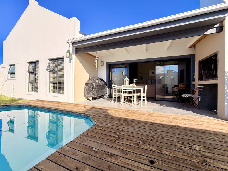 Outdoor entertainment area featuring a swimming pool with timber decking, a covered patio, and a built-in braai, perfect for alfresco dining.