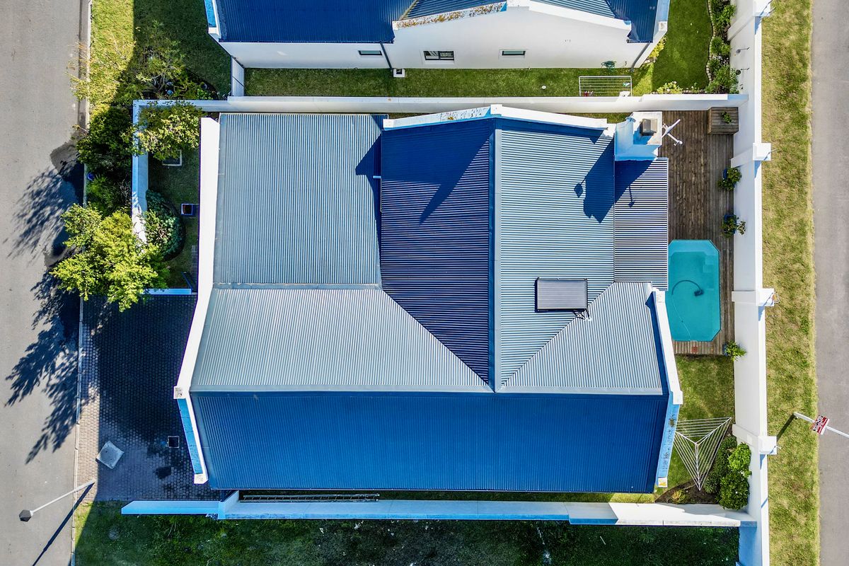 Aerial view of the property featuring a corrugated metal roof, solar panel, swimming pool, and timber decking within a secure boundary wall.