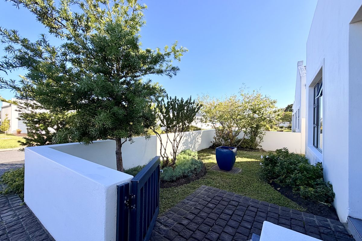 A well-maintained rear garden area featuring a neat lawn, established trees, and cobblestone paving enclosed by a white boundary wall.