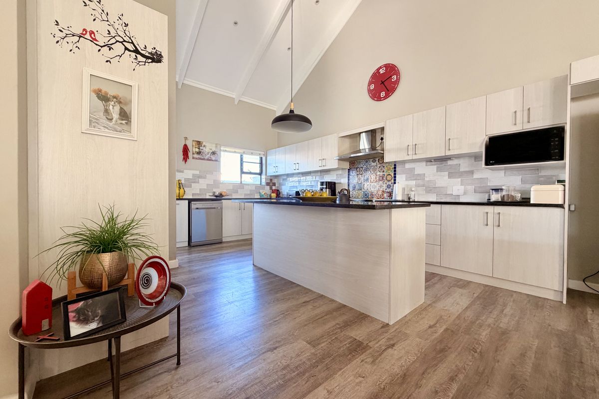 Modern kitchen featuring a central island, light wood-finish cabinetry, vaulted ceilings, and a decorative tiled backsplash, creating a bright and functional culinary space.