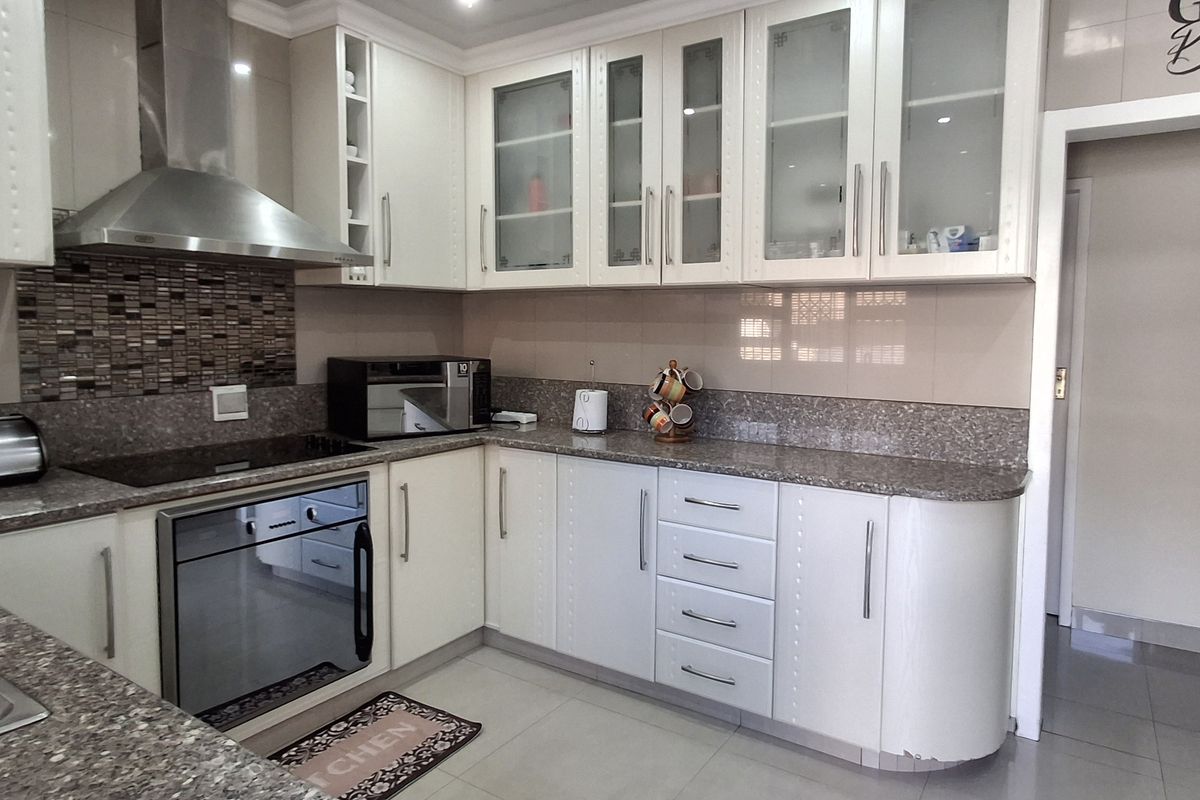 A well-maintained kitchen featuring white cabinetry, granite countertops, a mosaic tile backsplash, and integrated stainless steel appliances.
