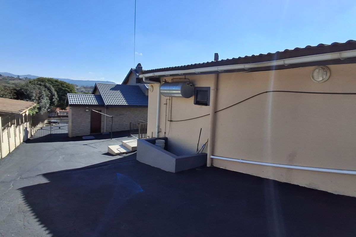 Rear exterior view showing an asphalt driveway, external geyser unit, and concrete steps leading to the property.