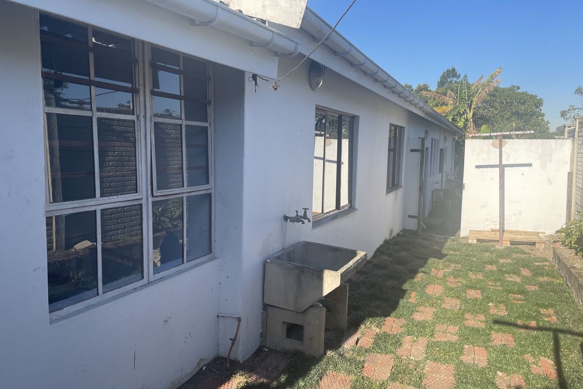 Rear exterior view of the townhouse featuring a concrete utility sink, paved walkway, and grass area with perimeter walling.