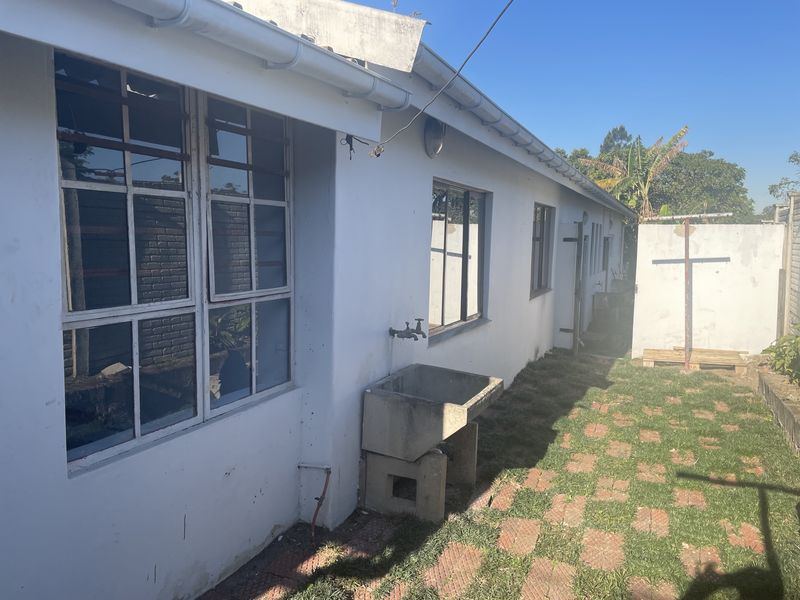 Rear exterior view of the townhouse featuring a concrete utility sink, paved walkway, and grass area with perimeter walling.