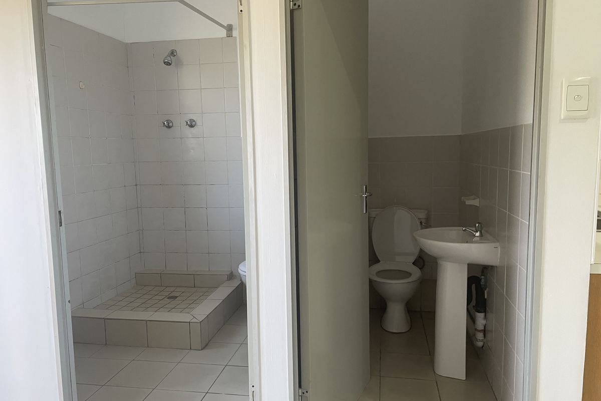 A functional bathroom featuring a separate shower cubicle with tiled surround and a pedestal basin with a toilet.