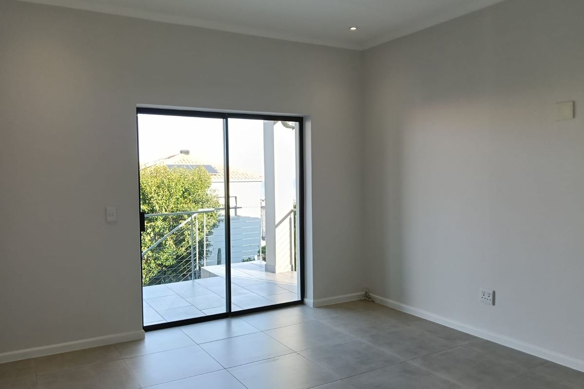 A bright, empty living room featuring neutral tiled flooring, recessed lighting, and a sliding glass door providing access to an outdoor patio area.